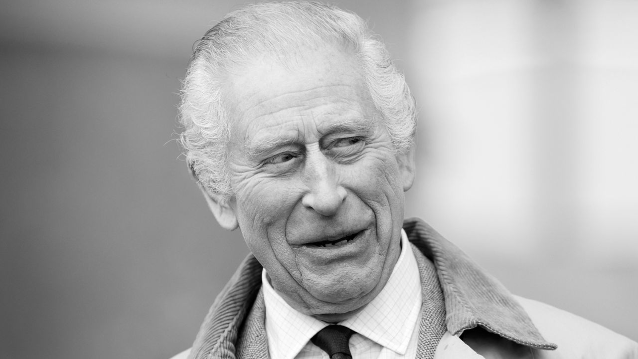 A black and white headshot of King Charles looking surprised wearing a tie and coat