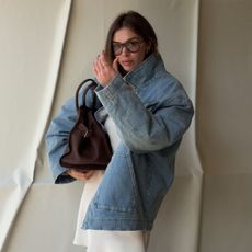 Woman wears denim jacket, white dress and carries brown bag