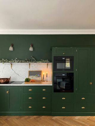 A kitchen with dark green cabinets and a white splashback