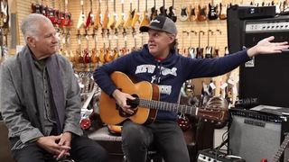 Norman Harris of Norman's Rare Guitars wears a gray scarf and jacket as he sits with regular Joe Bonamassa, who's wearing a ball cap, a blue hoody, and is playing a very nice vintage Martin 000 acoustic guitar.