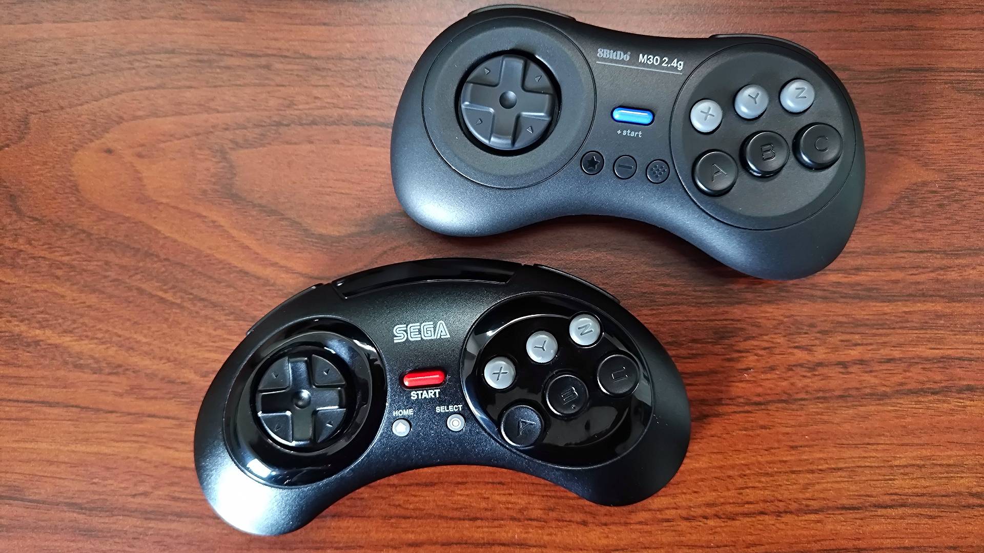 8Bitdo M30 on top and Retro-Bit Sega Mega Drive wireless controller on bottom sitting on woodgrain desk.