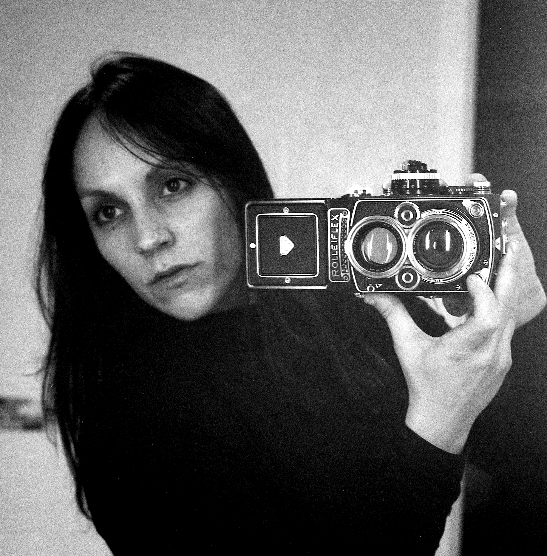 A person holds a vintage Rolleiflex camera in a black and white setting