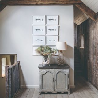 A rustic hallway with a staircase and fish prints hanging on the wall