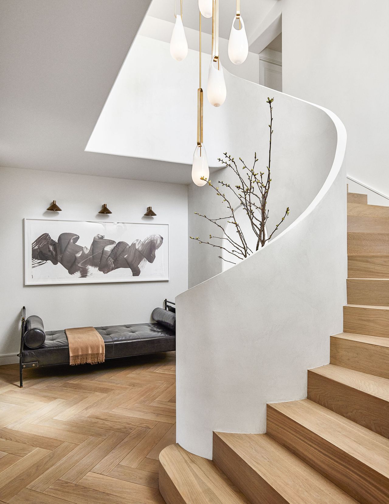 A modern curved white stairway with wooden steps and a black leather couch in the entry hall