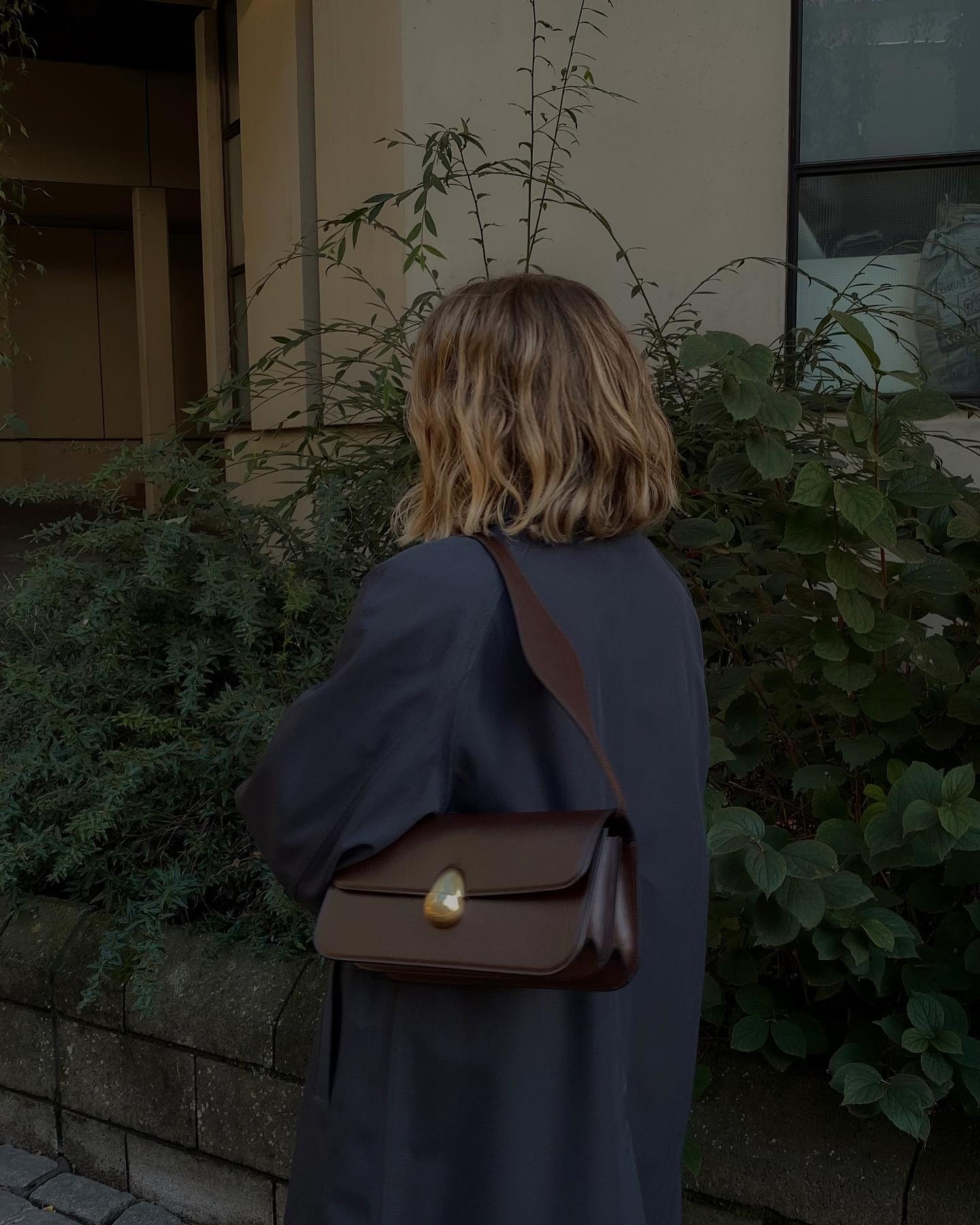 Influencer @brittanybathgate wears a navy coat with a brown leather baguette bag.