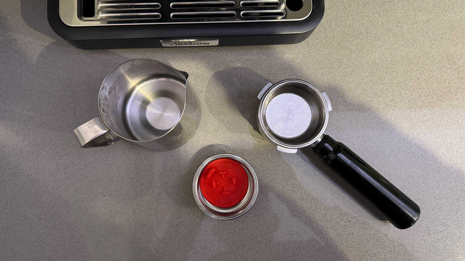 A stainless-steel milk jug, portafilter and single wall filter basket supplied with the Sunbeam Origins Classic Espresso Machine.