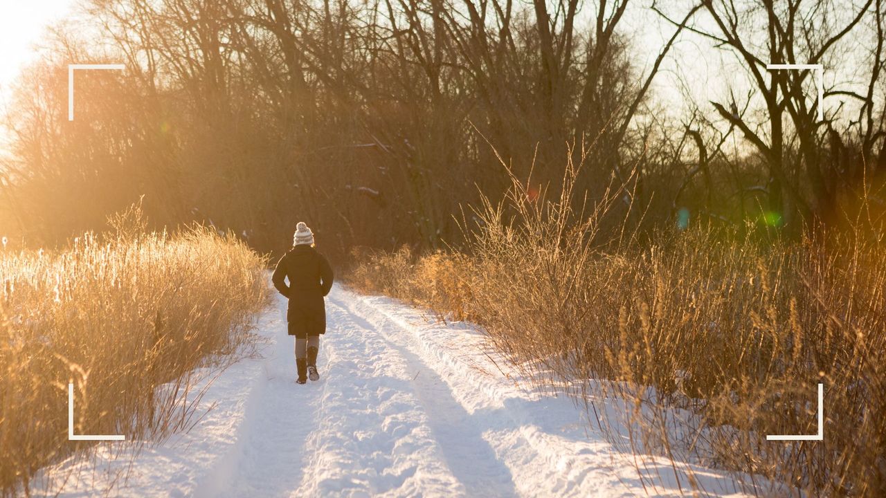 Woman walking away from the camera across snowy pathway, wearing red hat and coat, practising walking meditation