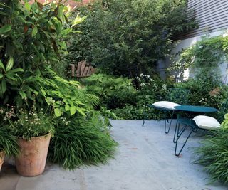 A small patio with lush planting on the boundaries and in pots with a small bistro furniture set
