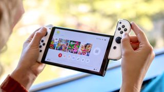 Nintendo Switch OLED held between two hands with one of the JoyCons being slid off