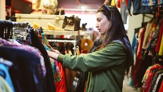 Vintage toned portrait of a young beautiful brunette woman in London second hand marketplace. She is wearing casual Autumn clothes, an olive green parka jacket, browsing through the stuff in the market.