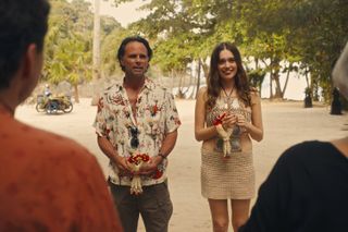 A couple dressed in summery, tropical clothes smiles at two people standing before them on a beach.