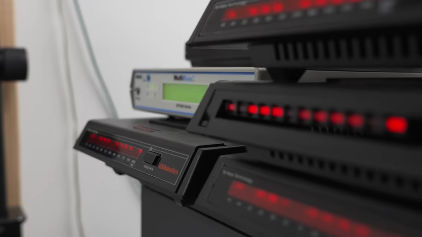A number of black 56 Kbps dial-up modems stacked on top of eachother, red lights blinking.
