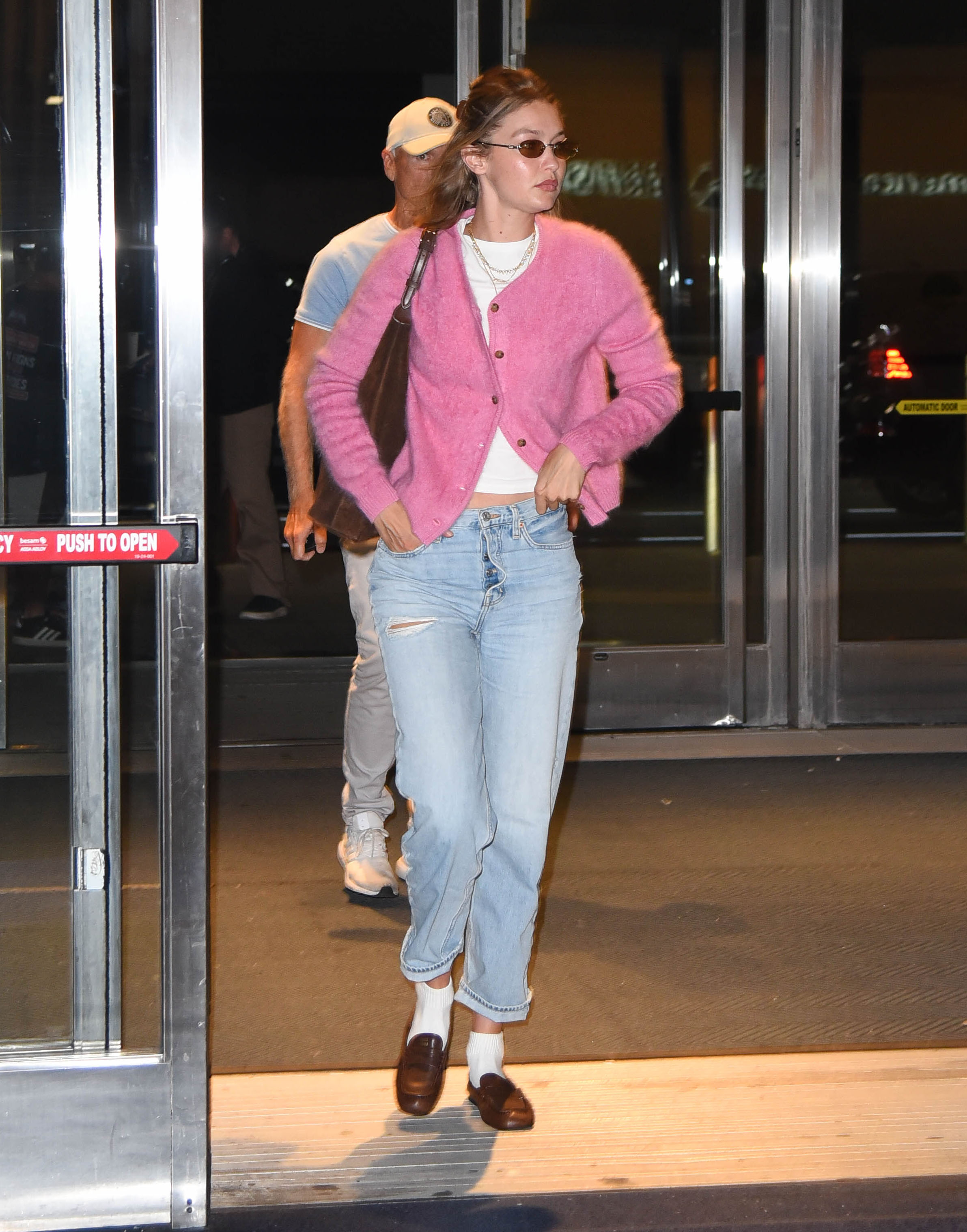 Gigi Hadid arrives at airport wearing a pink cardigan, white T-shirt, faded jeans, brown loafers and white socks