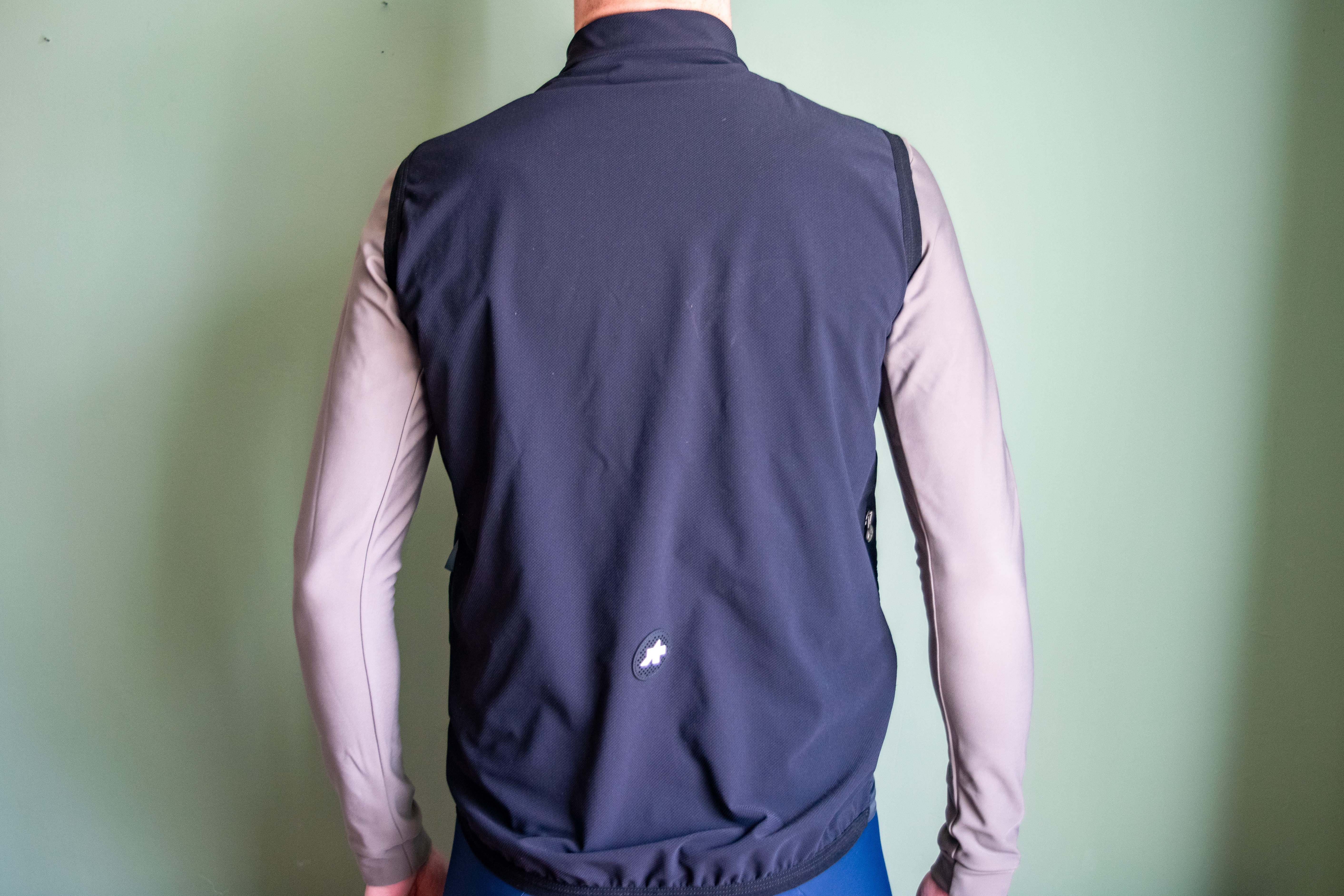 A man wearing a black Assos Tactica gilet over a grey long sleeve shirt