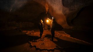Two explorers holding a kerosene lamp inside a massive, million-year-old dark cave.