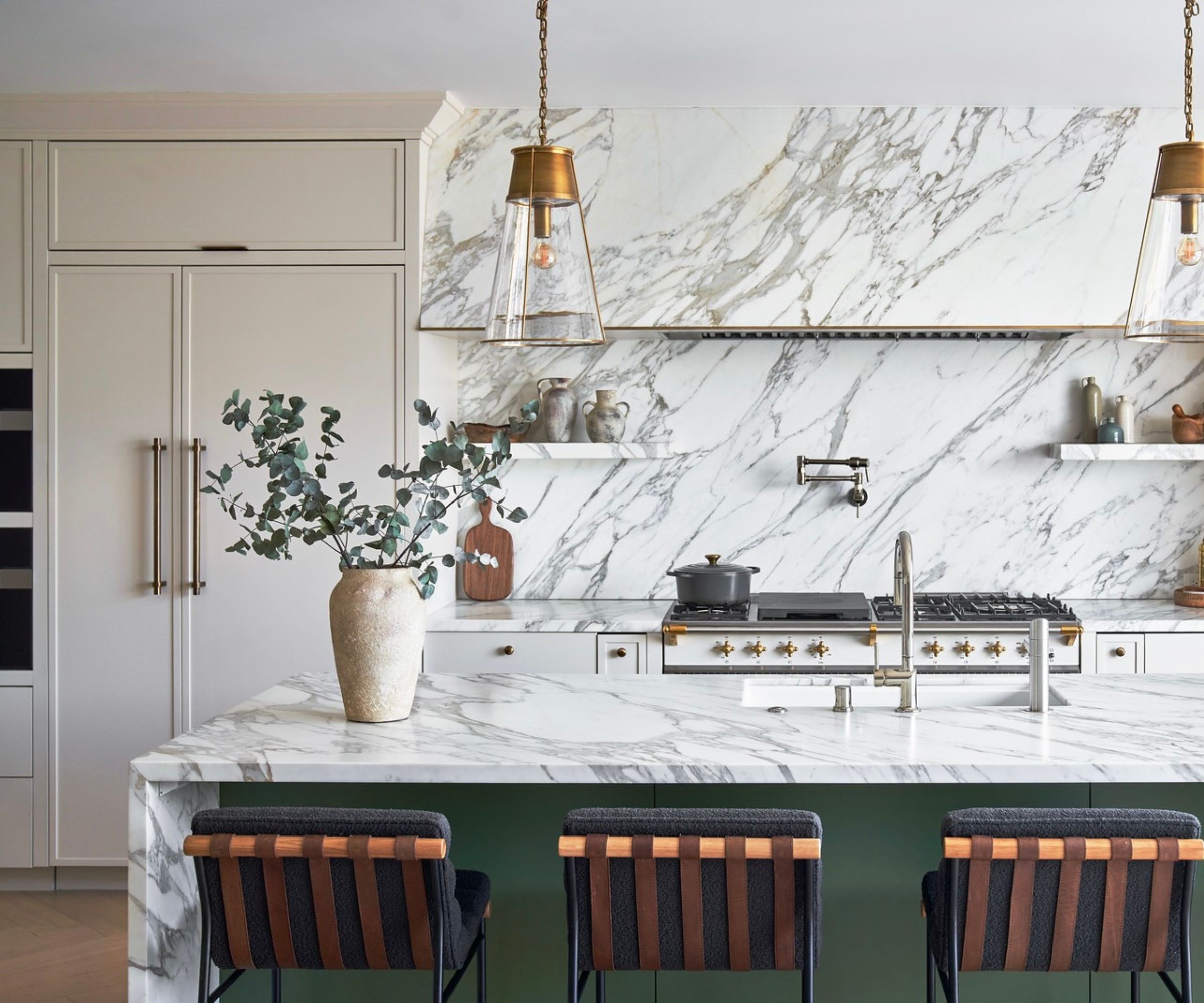 A marble and beige kitchen with pops of green on the island