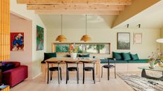Dining area of an open-plan space with built-in dining bench with storage, light wood table, black chair, double pendant lights, exposed wood ceiling and rafters