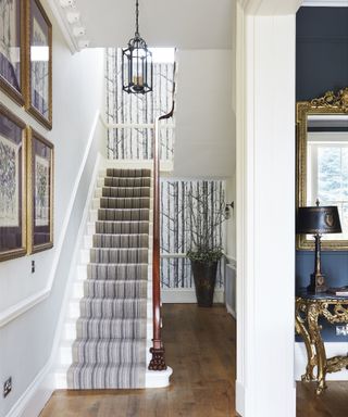 A hallway wallpaper idea with striped stair runner carpet and silver birch print wallpaper that runs across two levels