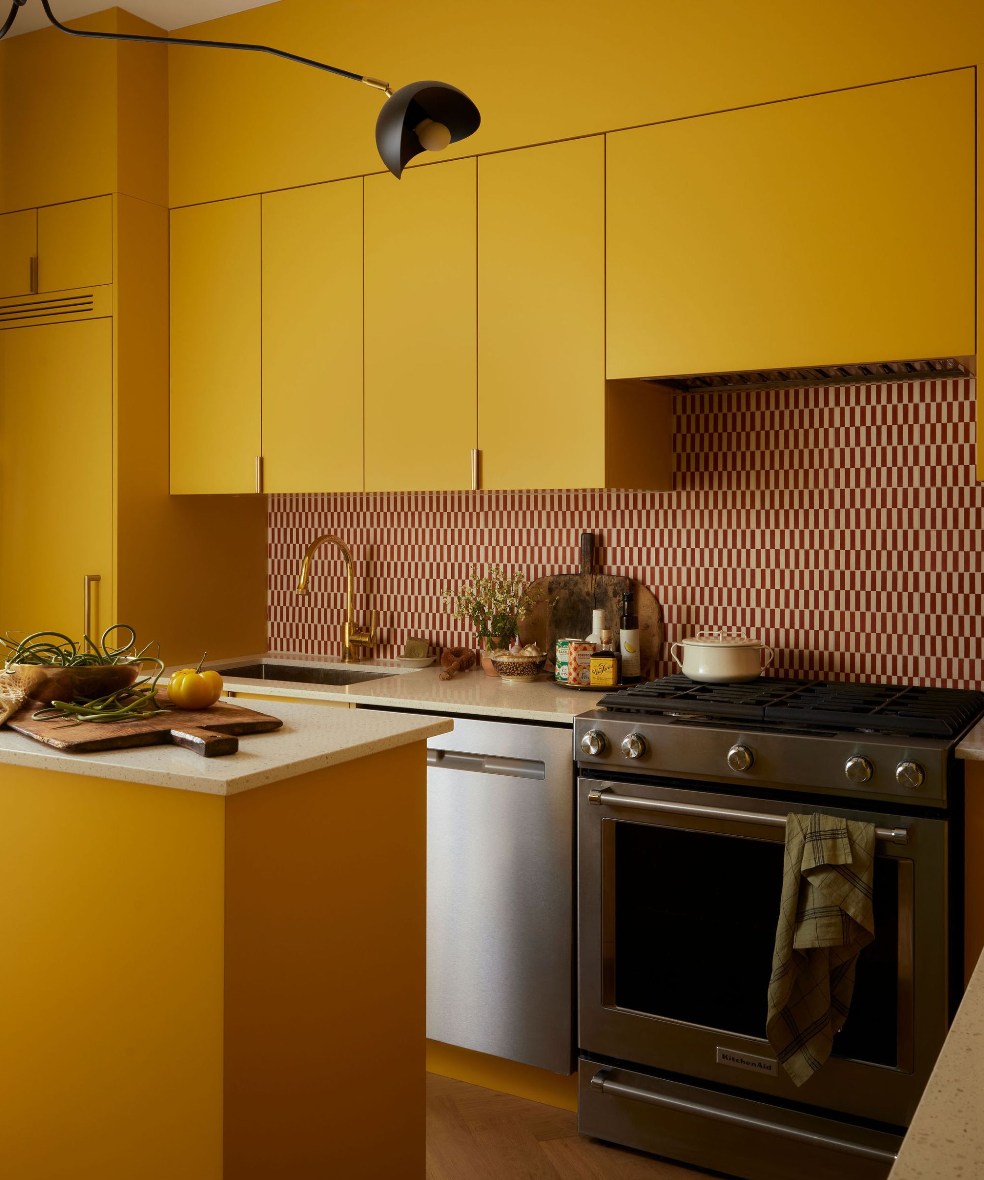 A modern kitchen featuring bright yellow cabinets, a stainless steel stove, and a red and white patterned backsplash