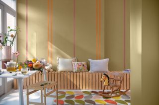 A yellow / green beige study with a wooden bench, patterned rug, and orange and purple accent stripes on the wall