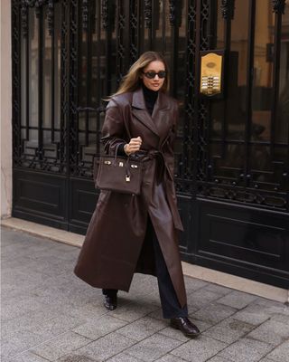 Lovisa wears a black turtleneck, black jeans, flats, an hermes bag, and a brown leather trench coat.