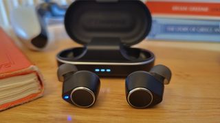 Cambridge Audio Melomania M100 wireless earbuds with their charging case on a wooden table