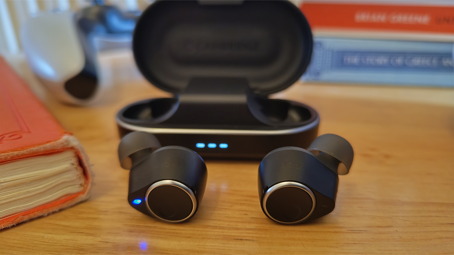 Cambridge Audio Melomania M100 wireless earbuds in front of case on wooden table