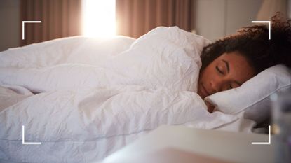 Woman lying on her side asleep peacefully in bed with sunlight coming in through the open curtains, representing what position is best to sleep in hot weather