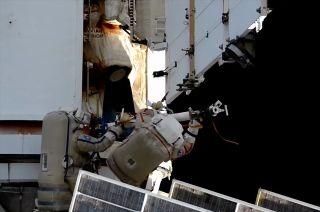 two cosmonauts wearing white spacesuits conduct a spacewalk outside the international space station.