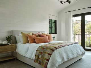 primary bedroom with peach colored pillows and paneled white walls french windows and balcony