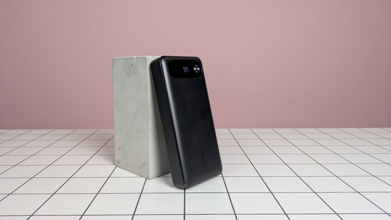 Anker 20,000mAh 87W Power Bank leaning on plinth on desk, with pink background