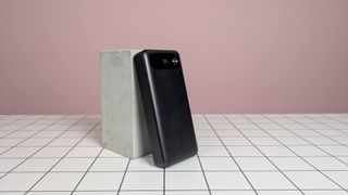 Anker 20,000mAh 87W Power Bank leaning on plinth on desk, with pink background