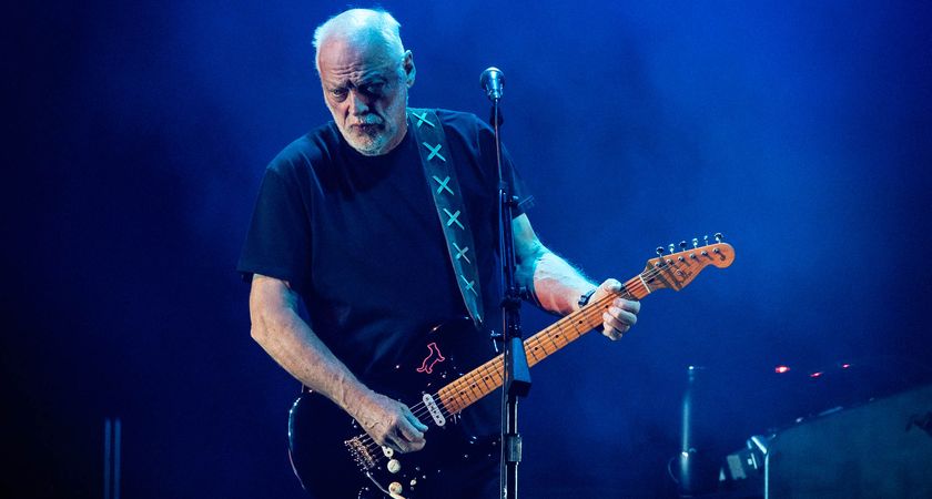 David Gilmour plays a Black Stratocaster onstage in New York, on a moody stage lit in dark blue.