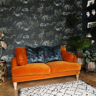 living room with dark palm wallpaper and orange sofa