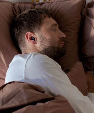 A man wearing Loop Dream earbuds and lying on brown bedding.