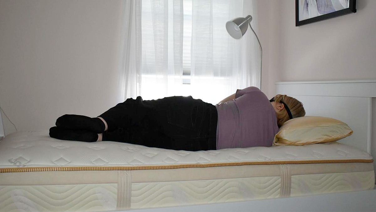 Tester with an eye mask sleeps on her side on a bare Saatva Memory Foam Hybrid Mattress; her back is facing the camera to show alignment and contouring.
