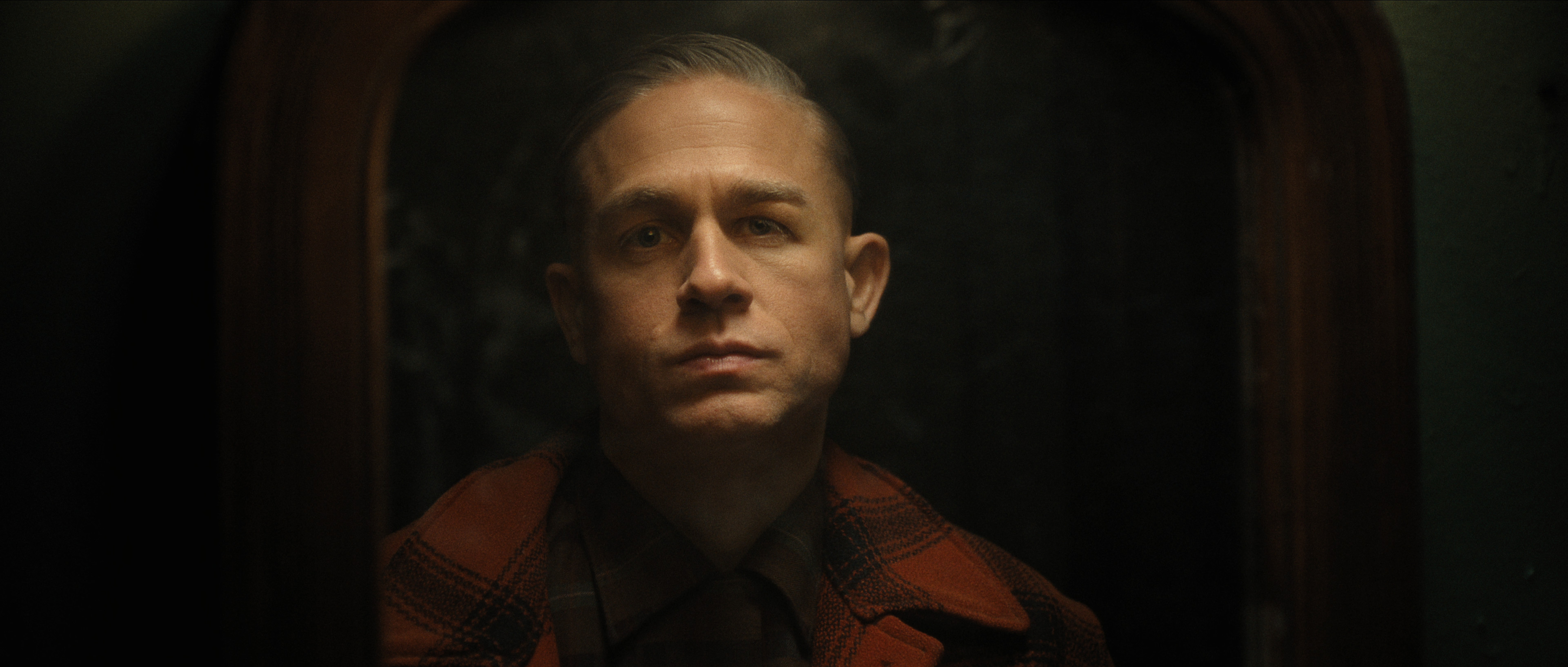 charlie hunnam as ed gein in a black lit photo wearing a red plaid jacket in monster