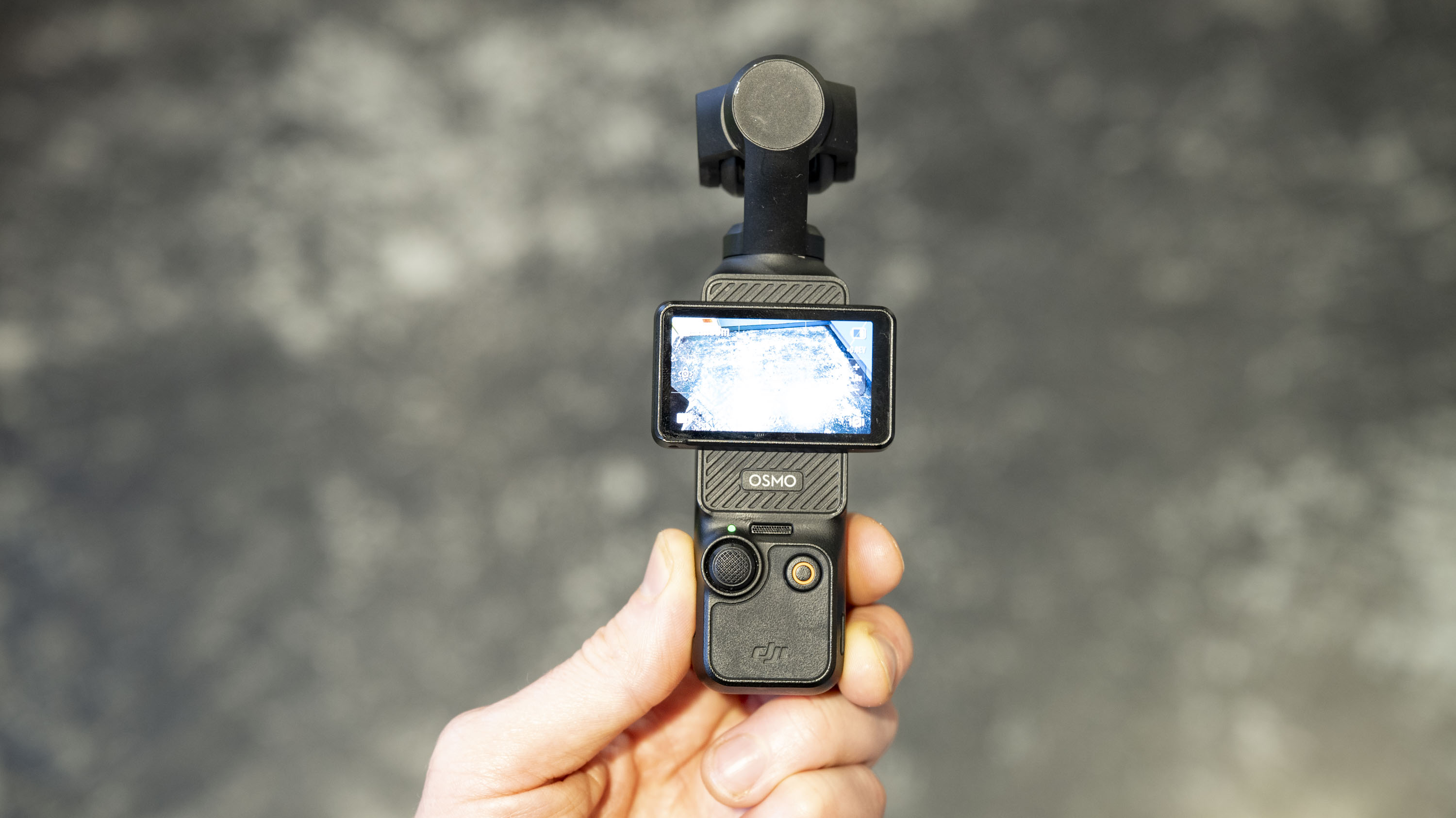 DJI Osmo Pocket 3 vlogging camera in user&#039;s hand, grey floor in background