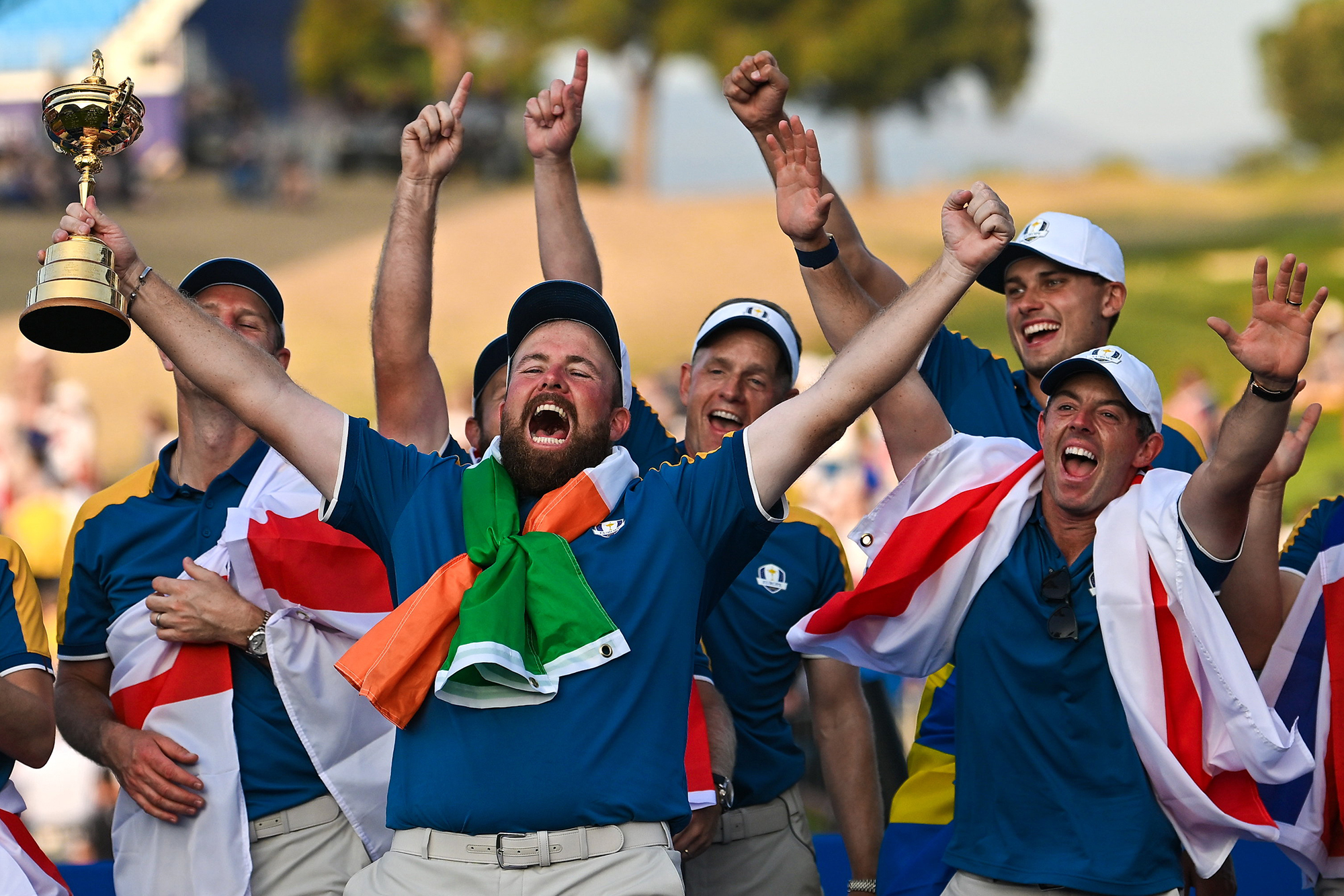 Shane Lowry lifting the Ryder Cup, with the flag of Ireland wrapped around his shoulders, in front of the victorious 2023 European Ryder Cup Team