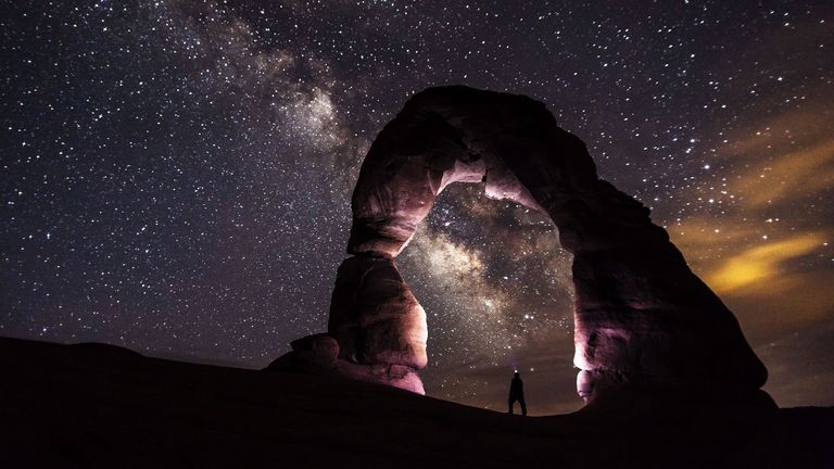 Person Standing Under A Rock Formation On A Starry Night