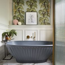 Blue bath in bathroom with white panelling behind it.