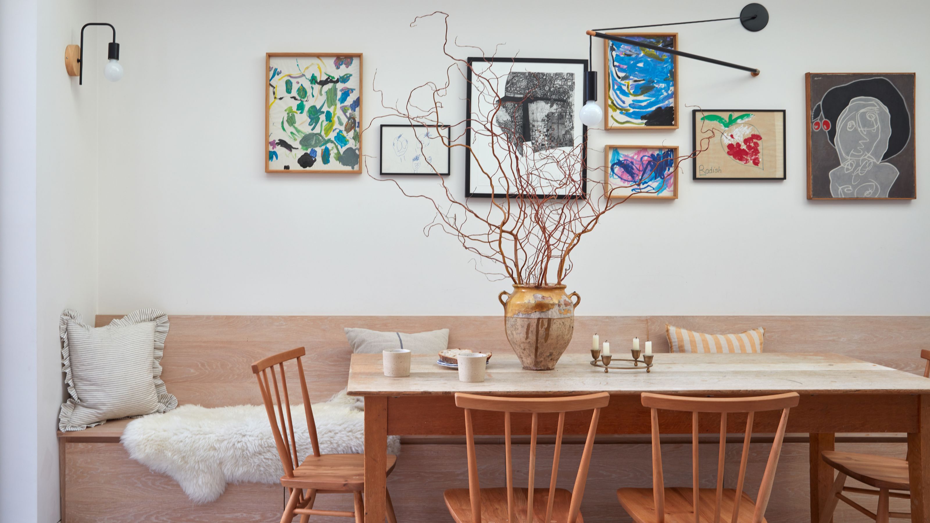 White painted dining room area with a gallery wall on the wall and wooden banquette seating behind a wooden table and chairs
