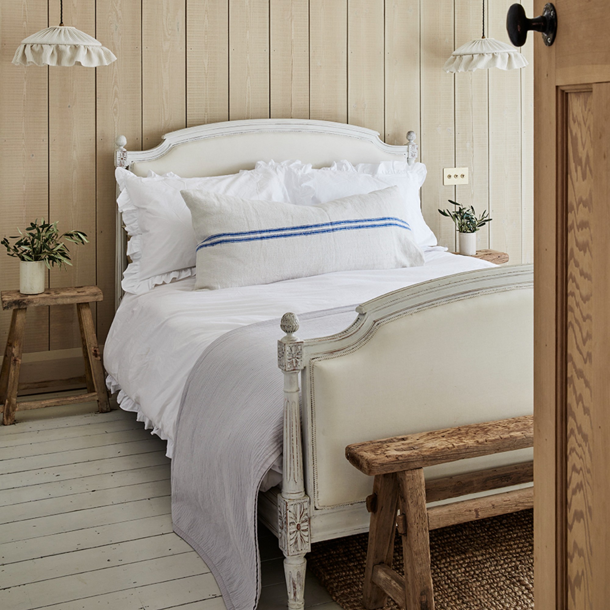 A rustic bedroom with a vintage bed frame, two ruffled pendant lamps and wood wall panelling