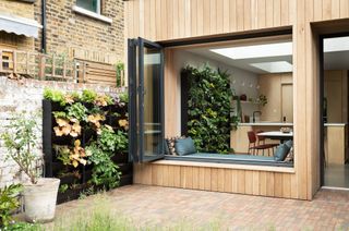 A timber clad extension with a large window that opens to reveal window seating