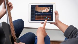 Two people use a guitar lessons app displayed on a white iPad