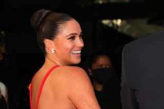 Meghan Markle in a red gown looking over her shoulder