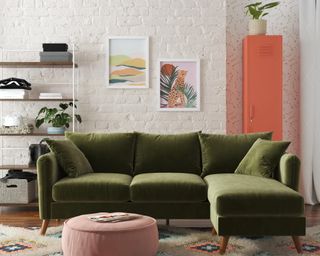 A small apartment living room with olive green velvet upholstered sofa, pastel pink upholstered ottoman, framed wall art, open shelving and coral colored locker storage unit