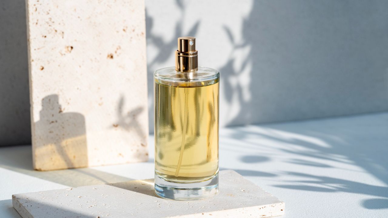 A perfume bottle on a white countertop with shadows of leaves behind it