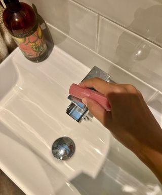 Person rubbing pink candle over over water stained bathroom faucet