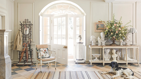 a white front entryway with a large door, a credenza with small statues on it, and an accent chair to the left